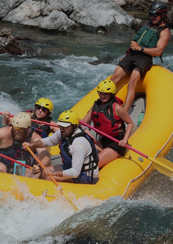 A group of rafters on white water, the guide is standing in the back of the boat.