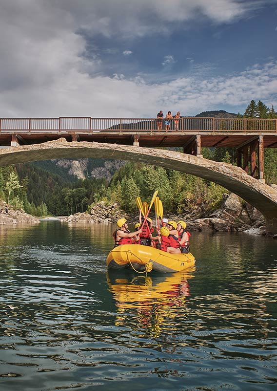 A group of rafters touch their paddles together as they float under a bridge.