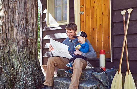 A dad and child sit on the steps of a wooden cabin.