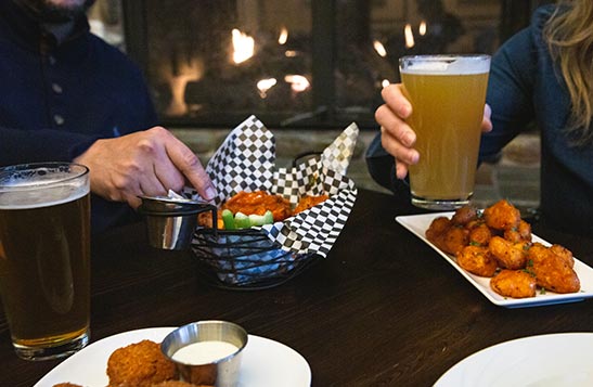 People taking wings out of a wing basket at a table with beer
