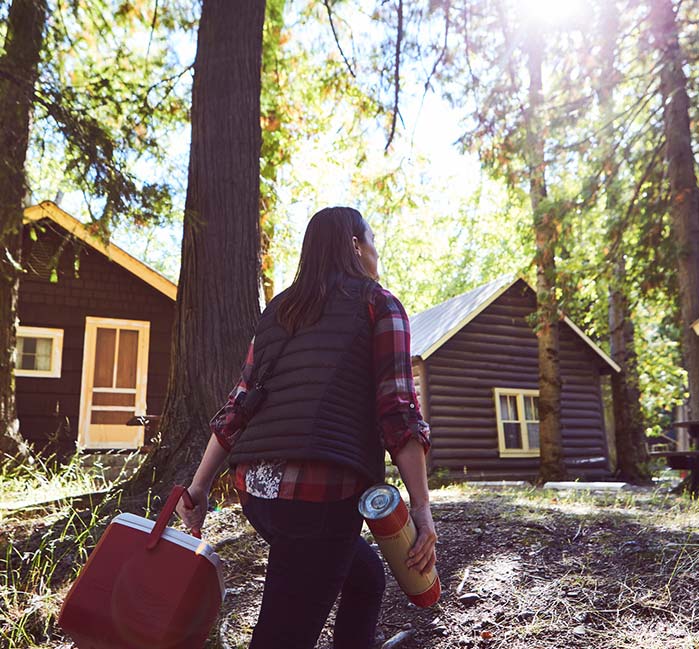 Woman walking in between trees, cabins in the background.