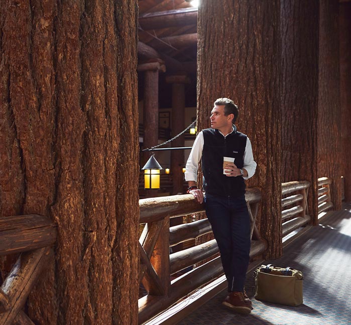 Man leaning against a wooden railing, holding coffee cup.