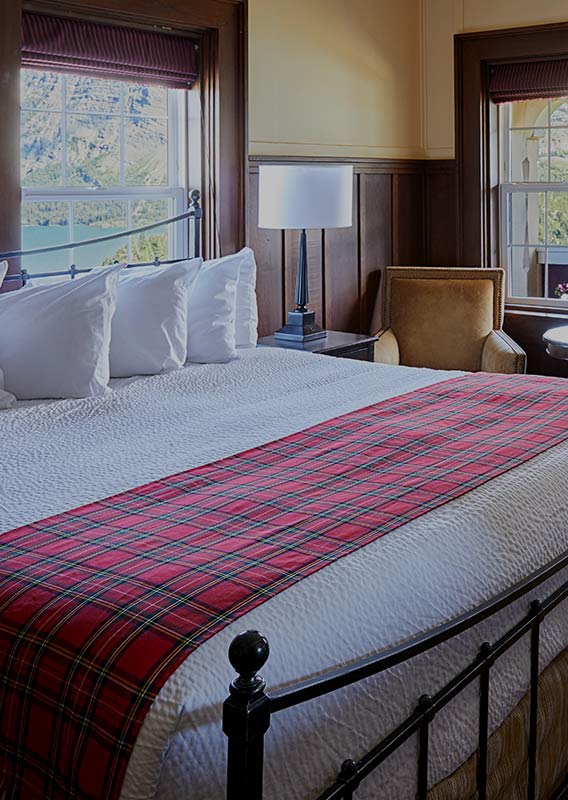 A hotel bed made in a corner room with windows overlooking a blue lake.
