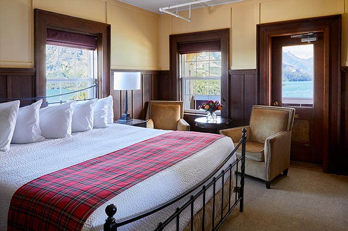 Well-appointed hotel room with one king bed, sitting area and views of Waterton Lake