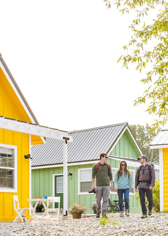 Three adults walking among yellow and green tiny homes