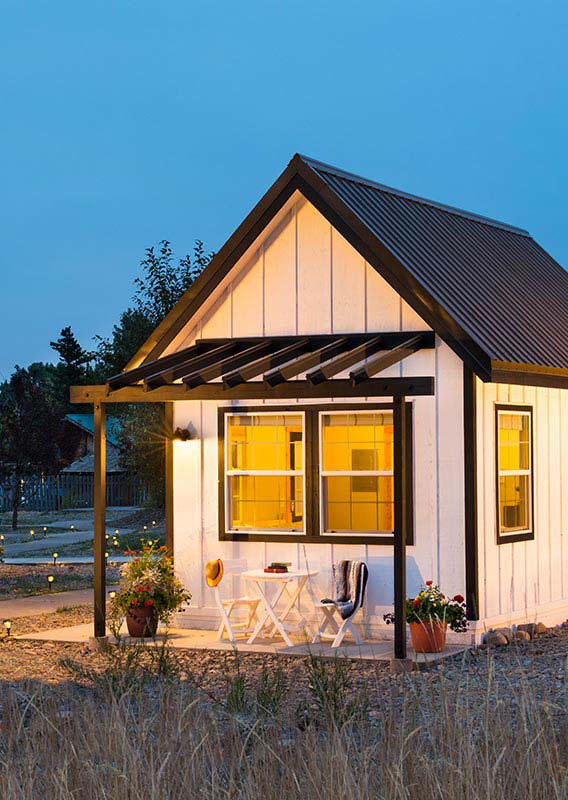 A white tiny home with an inviting porch at dusk