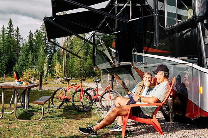 A couple sits in adirondack chairs next to their RV