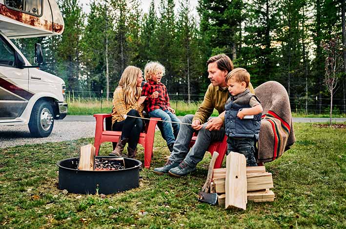 A couple with young children sit by a fire pit roasting marshmallows