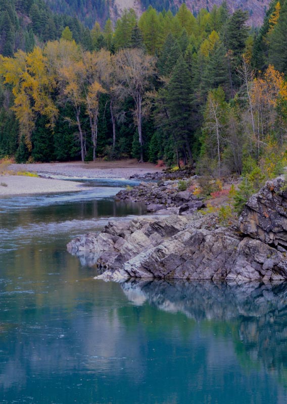 A blue river flows between rocky, tree-covered shores