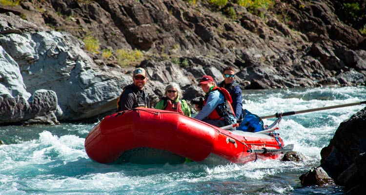 Four people ride a red raft on a river rushing between rocky banks.