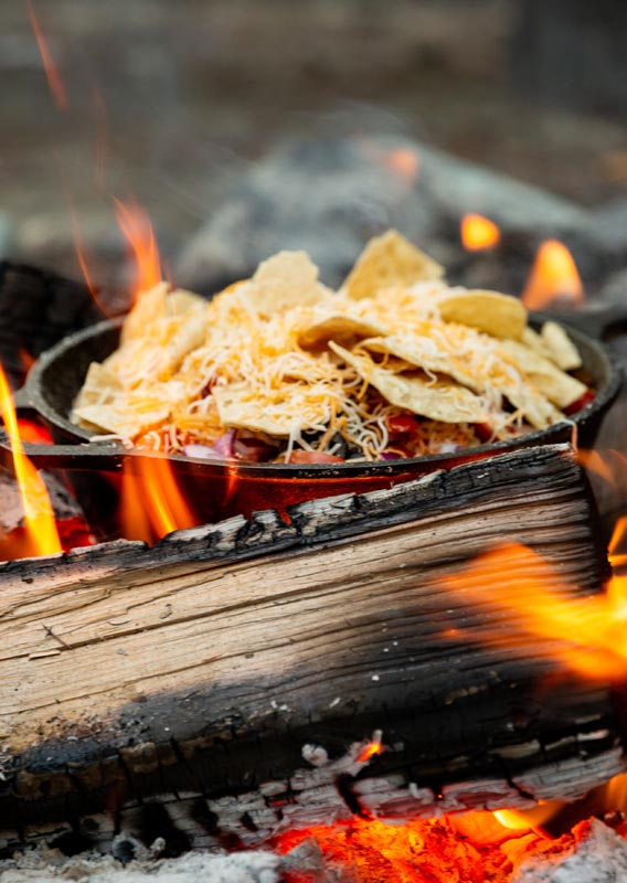 A cast iron pan of nachos cooking over a campfire