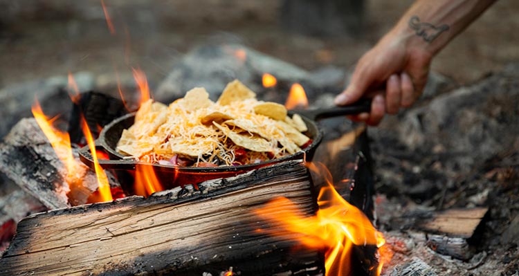A cast-iron pan of nachos roasting on a fire.