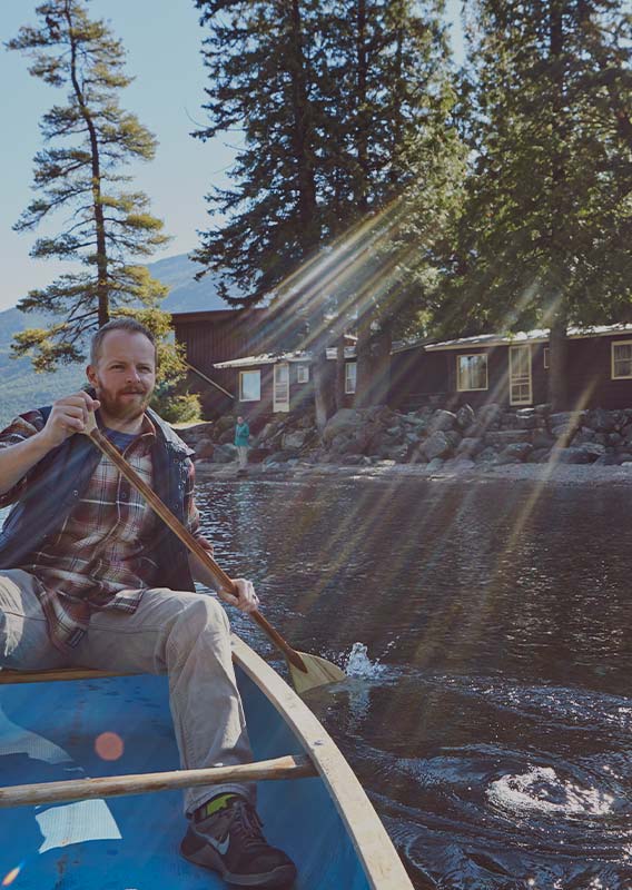 A man canoes close to the shore of a calm lake.