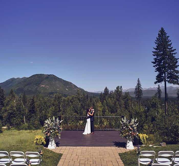 A bride and groom stand alone at an outdoor altar in summer.