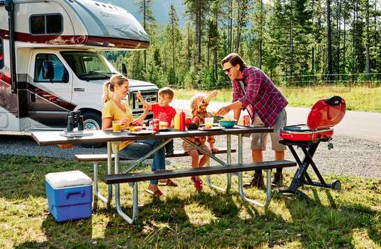 A family sitting at a picnic table outside next to their RV in spring.