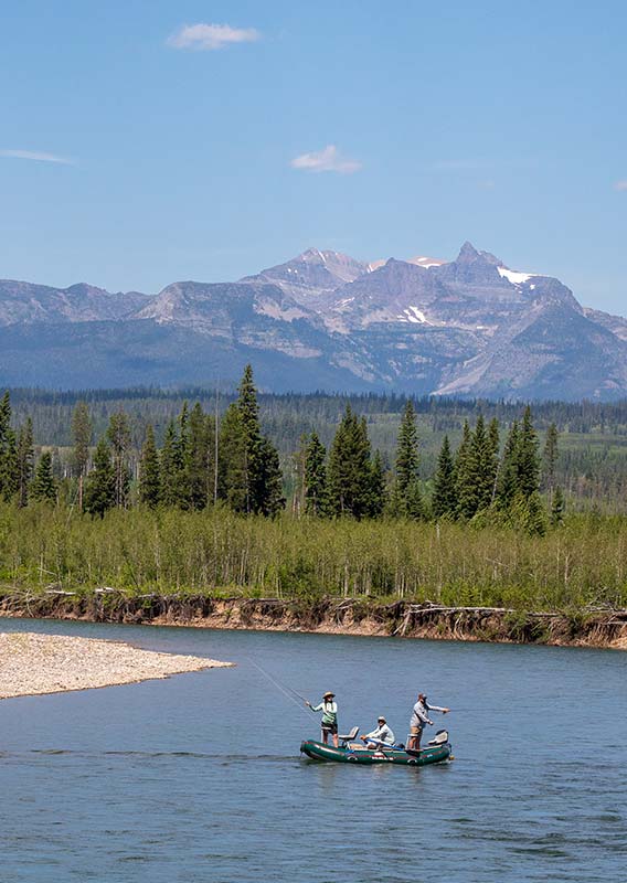 A fisher rafts along a river between forests.