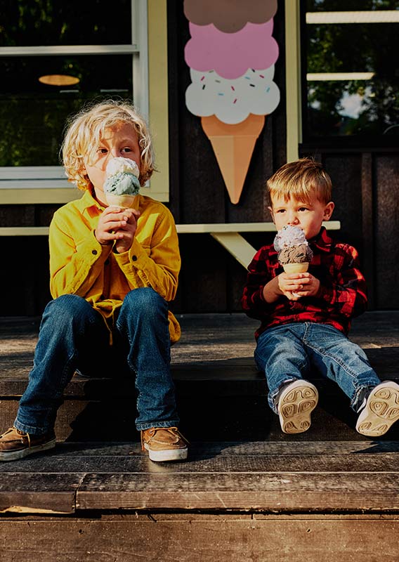 Two kids sit on wooden steps eating ice cream cones.