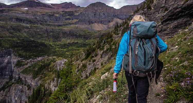 A hiker walks down a trail with bear spray in hand.