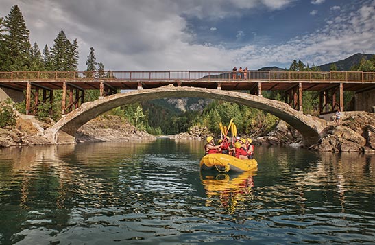 Rafters lift their paddles to cheer as they float under a bridge.