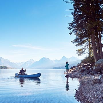 A canoe on still water with a person standing by the shoreline.