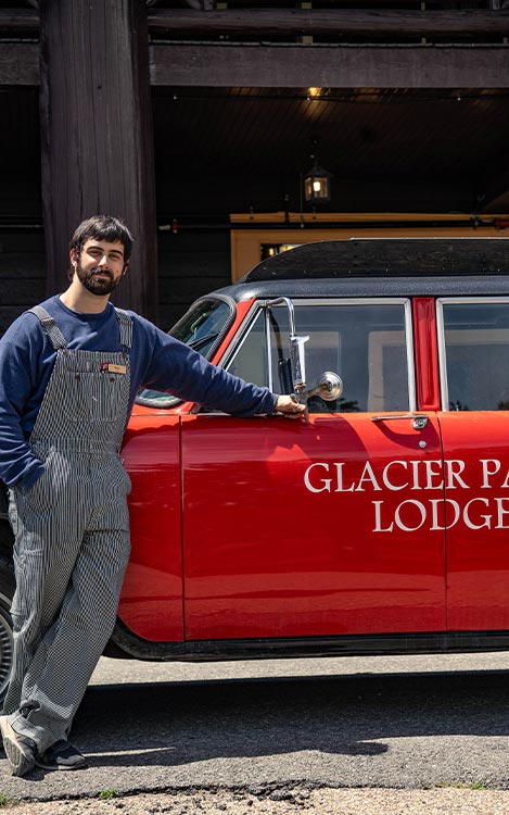 A car bellhop stands outside a historic-style red car.