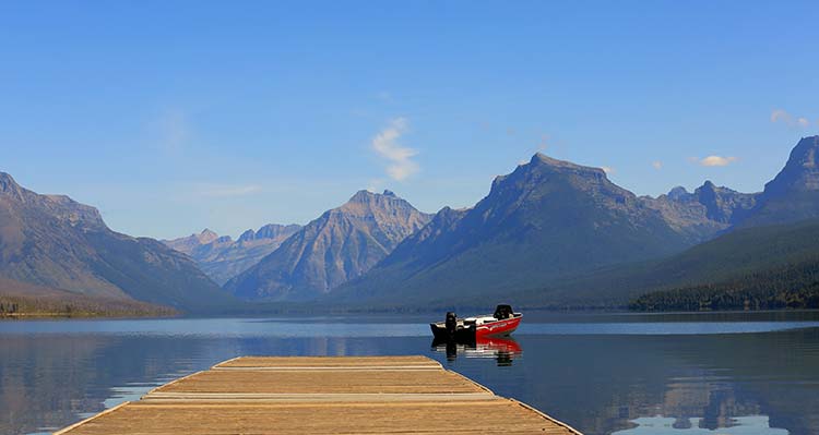 A still lake dock in front of a mountain range.