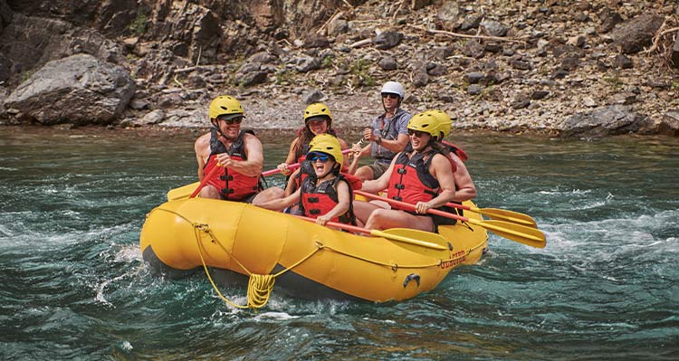 A group of people paddle down a calm river in a yellow raft.