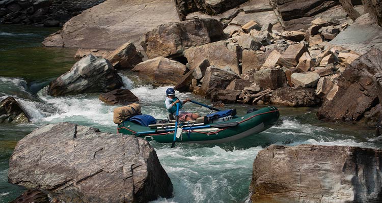 A rafting guide navigates rapids in a rocky river.