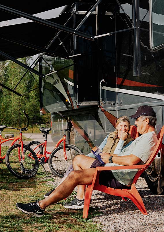 Two people sit under an RV awning.