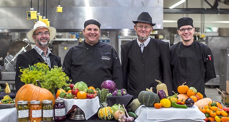 A group of farmers and chefs stand at a table of produce.